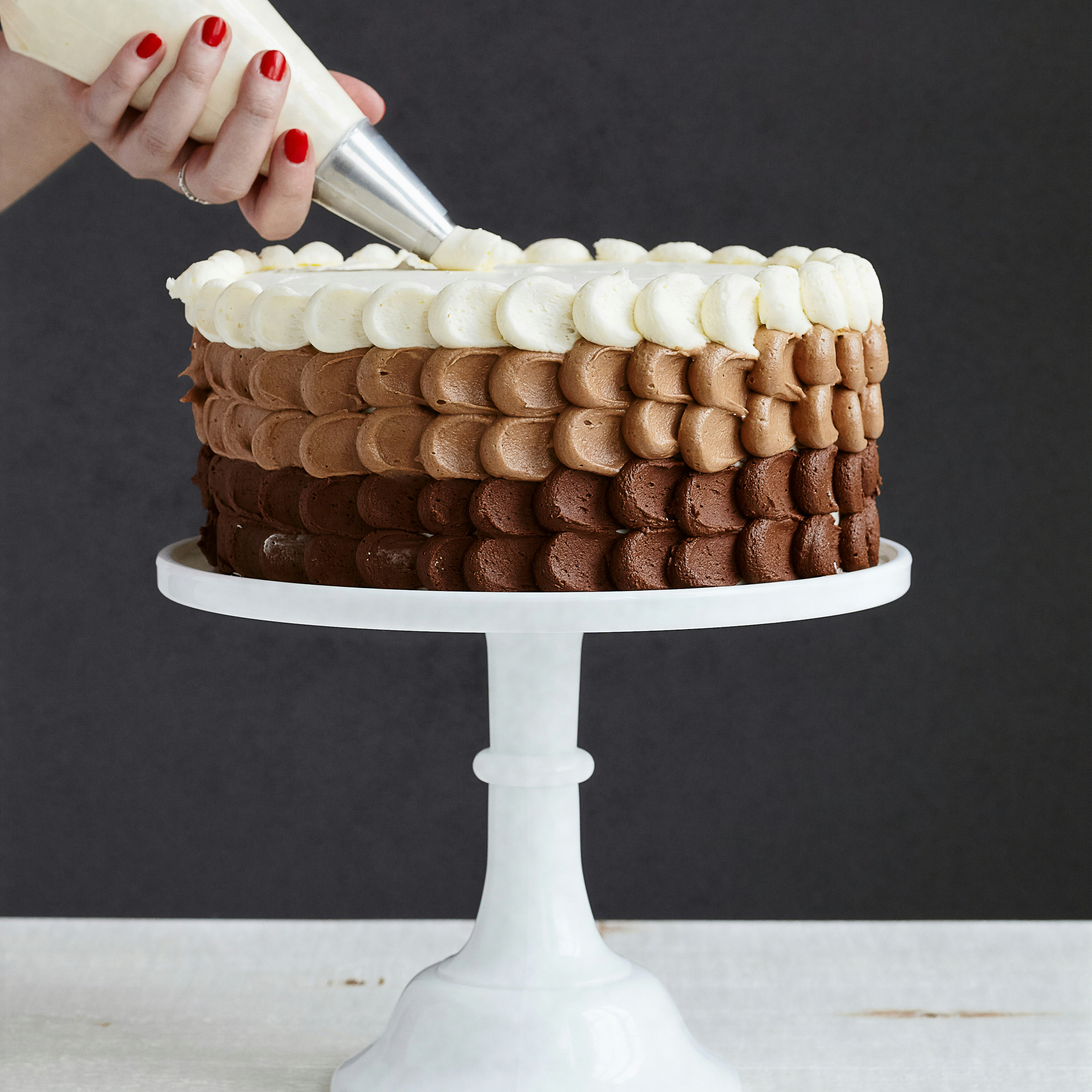 chocolate cake being decorated by hand with brown and white icing on a marble countertop