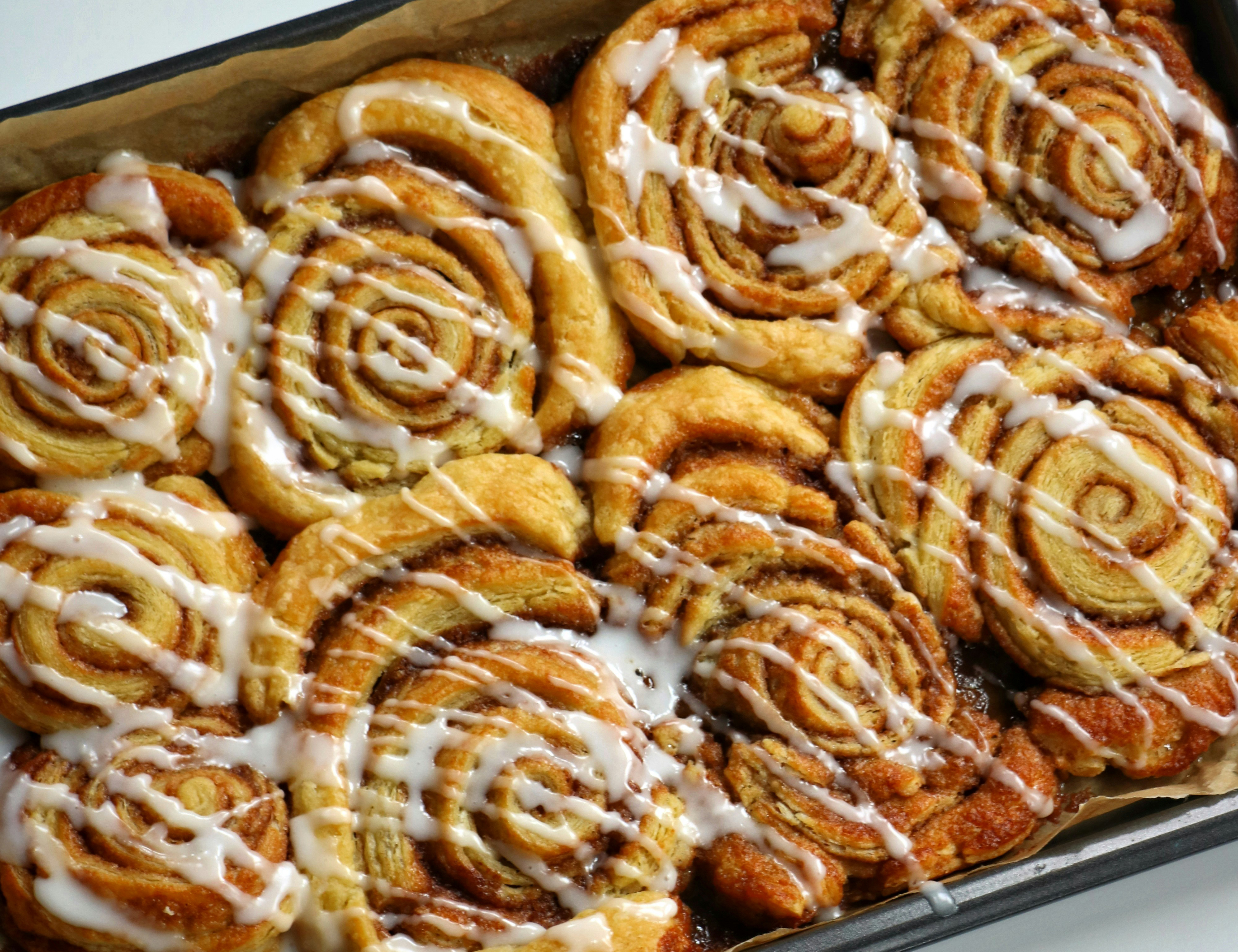 pan full of cinnamon rolls with drizzled icing on a white countertop
