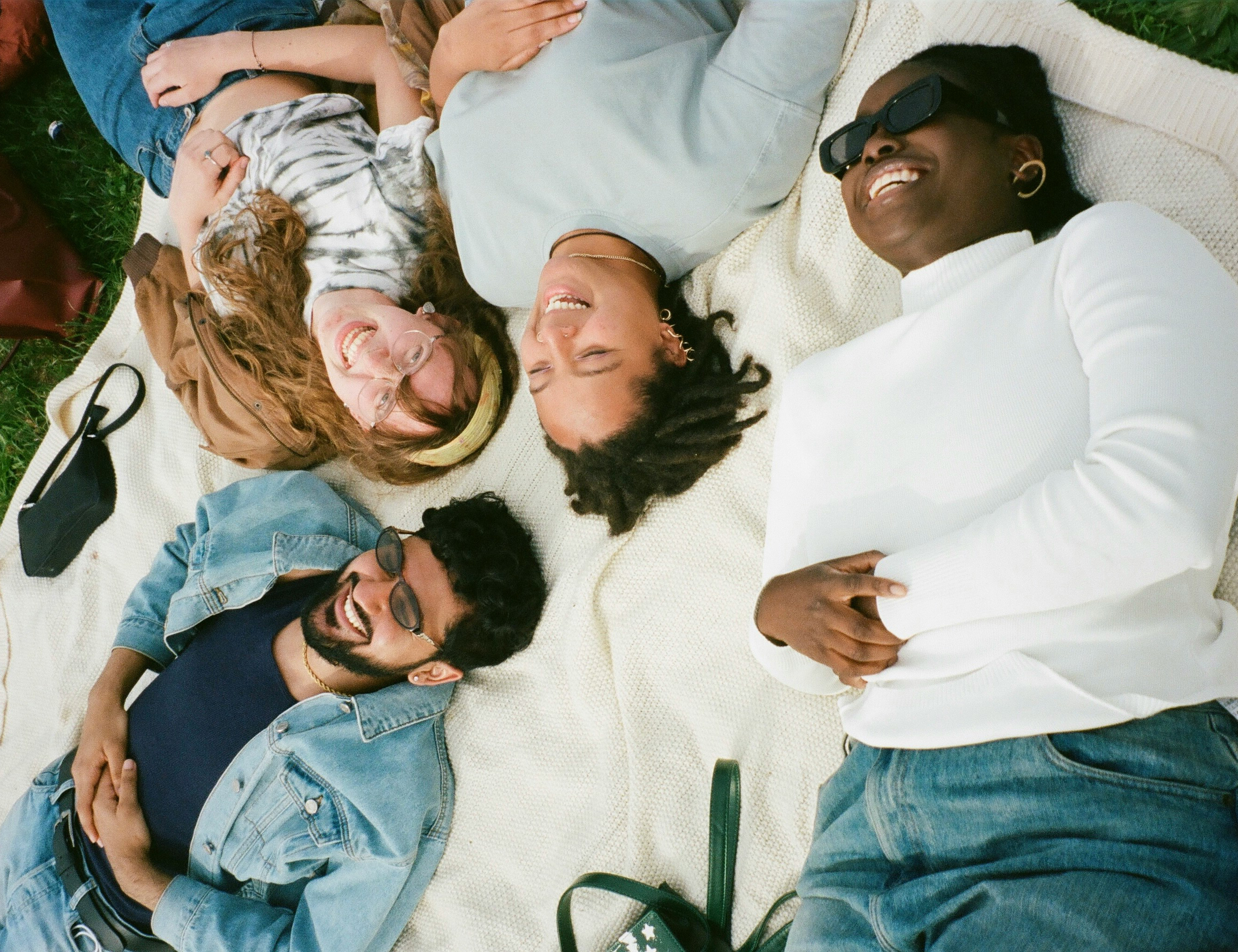 people laughing and talking together in a group on a white blanket on grass outside